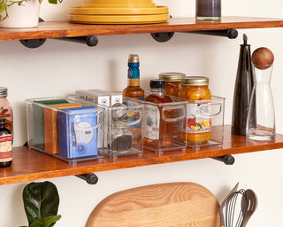 Several plastic bins, full of pantry items, on a wooden shelf